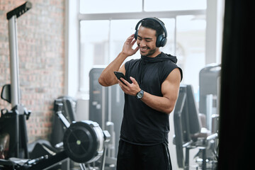 Listening, headphones and man with cellphone in gym, athlete and ready for workout, fitness and training. Health club, guy and routine of exercise in morning, ambition and preparing of competition