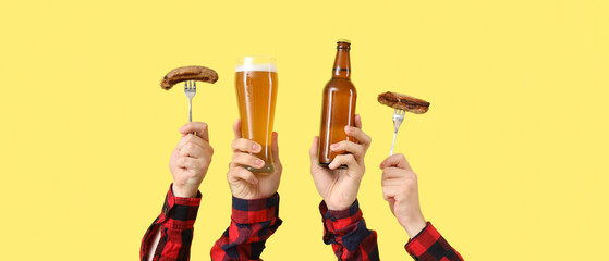 Hands with beer and sausages on yellow background