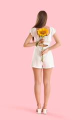 Young woman with beautiful sunflower on pink background, back view