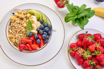 Granola with strawberries, kiwi, banana and blueberries in a round plate on a white table. Healthy and tasty food