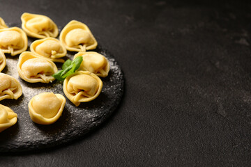 Board with raw dumplings and basil on black background