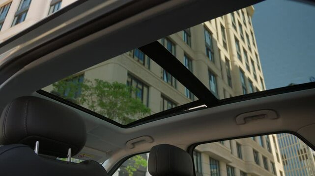 View of a transparent two-section car hatch or sunroof through which you can see the blue sky and a modern building in the metropolis.