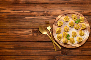 Board with raw dumplings and basil on wooden background