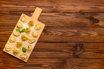 Board with raw dumplings and basil on wooden background
