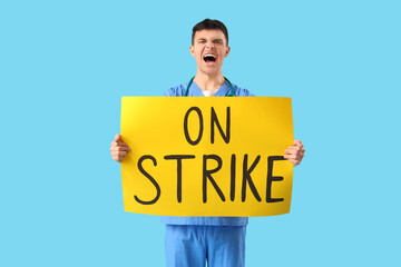 Protesting male doctor holding placard with text ON STRIKE against blue background