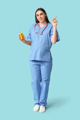 Beautiful young pregnant doctor holding jar with fish oil pills pointing at something on blue background