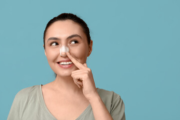 Young woman pointing at bandaged nose on blue background. Plastic surgery concept