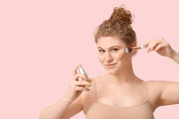 Naklejka premium Beautiful young woman with bottle of foundation and makeup brush on pink background