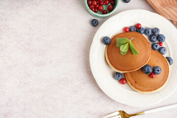 Plate with delicious pancakes and berries on white table