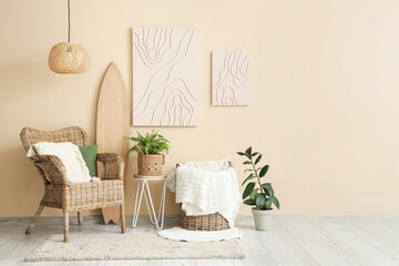 Interior of stylish living room with wicker armchair, surfboard and paintings hanging on beige wall