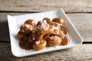 Tasty candies, caramel sauce and salt on wooden table, closeup