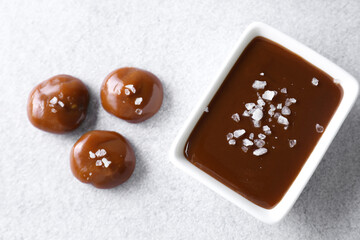 Tasty candies, caramel sauce and salt on light grey table, top view