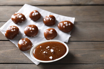 Tasty candies, caramel sauce and salt on wooden table