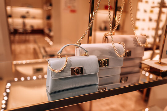 Furla blue and white handbags with golden chain on a stand in a shopping mall. Luxury accessories