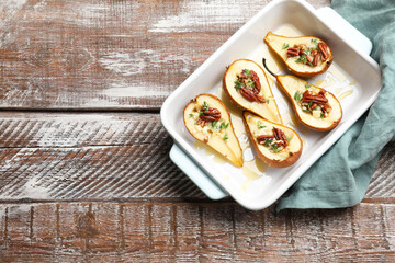 Tasty baked pears with nuts, blue cheese, thyme and honey in baking dish on wooden table, top view. Space for text