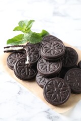 Tasty sandwich cookies and mint on white marble table