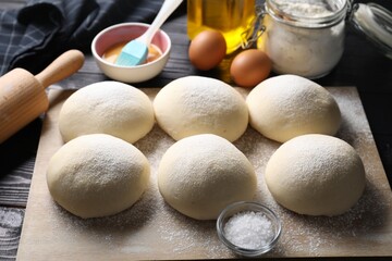 Raw dough balls, yolk, salt, flour, eggs and rolling pin on black wooden table