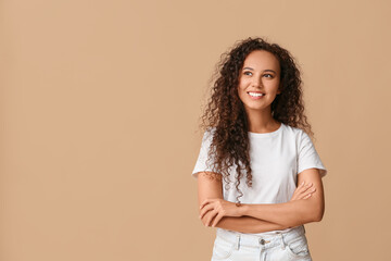 Happy young African-American woman on beige background