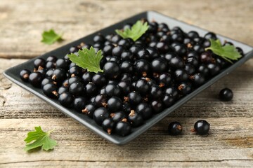 Ripe black currants and leaves on wooden table, closeup