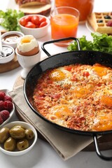 Tasty shakshouka in frying pan and other meals served for breakfast on white table, closeup