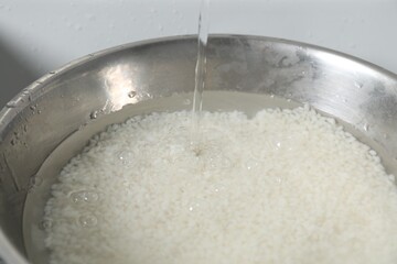 Pouring water into bowl with rice in sink, closeup