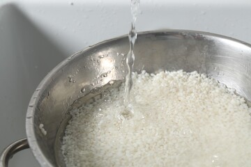 Pouring water into bowl with rice in sink, closeup