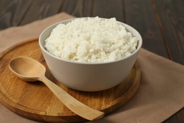 Delicious boiled rice in bowl and spoon on wooden table