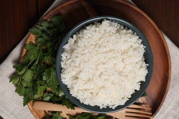 Delicious boiled rice served with parsley on wooden table, top view