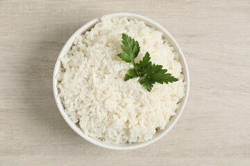 Delicious boiled rice in bowl and parsley on wooden table, top view