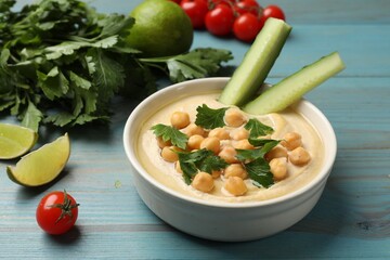 Tasty hummus with chickpeas in bowl and fresh products on light blue wooden table, closeup