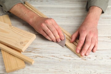 Man polishing wooden plank with sandpaper at table, closeup