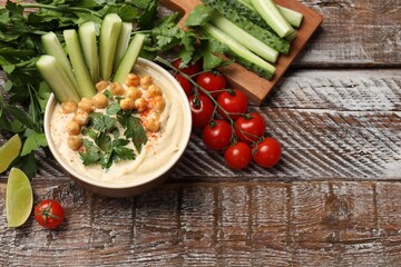 Tasty hummus with chickpeas in bowl and fresh products on wooden table, flat lay. Space for text