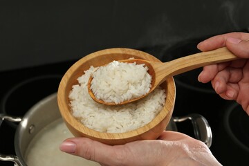 Woman taking boiled rice from pot into bowl, closeup