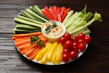 Tasty homemade hummus and different vegetables on dark wooden table
