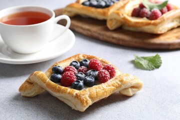 Tasty puff pastries with berries and tea on white table, closeup