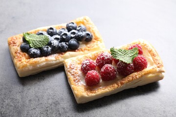 Tasty puff pastries with berries on grey table