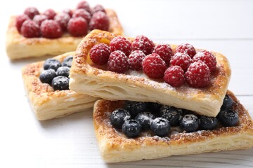 Tasty puff pastries with berries on white wooden table, closeup