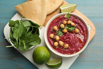 Tasty beet hummus with chickpeas in bowl served on light blue wooden table, flat lay