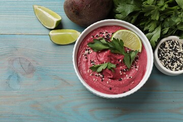 Tasty beet hummus in bowl and fresh ingredients on light blue wooden table, flat lay. Space for text