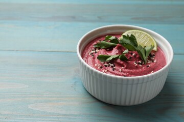 Tasty beet hummus with parsley and lime in bowl on light blue wooden table. Space for text