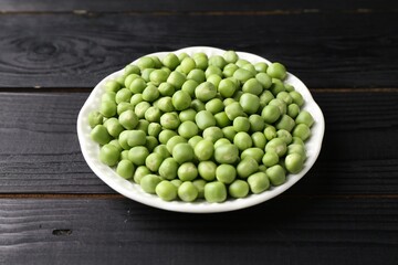 Fresh green peas in bowl on black wooden table