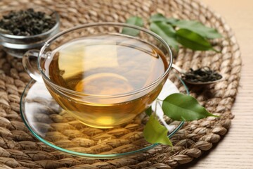 Refreshing green tea in cup and leaves on wooden table, closeup