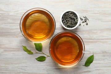 Refreshing green tea in cups and leaves on light wooden table, flat lay