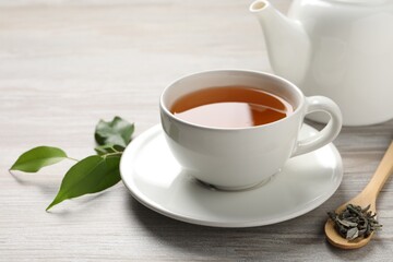 Refreshing green tea in cup, spoon and leaves on grey wooden table, closeup