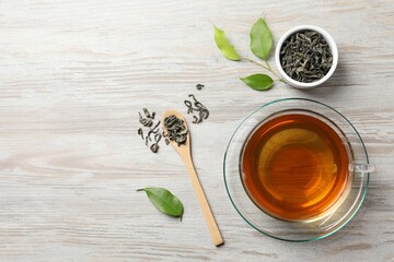 Refreshing green tea in cup, spoon and leaves on light wooden table, flat lay. Space for text