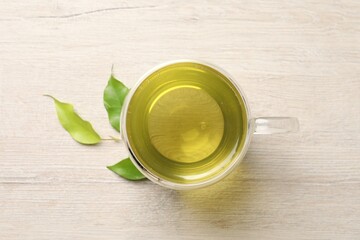 Refreshing green tea in cup and leaves on wooden table, top view
