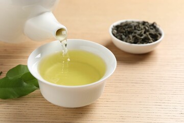 Pouring refreshing green tea into cup at wooden table, closeup