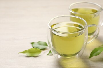 Refreshing green tea in cups and leaves on wooden table, closeup. Space for text