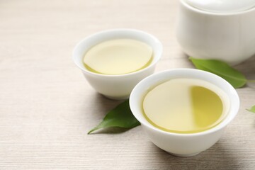 Refreshing green tea in cups and leaves on wooden table, closeup