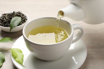 Pouring refreshing green tea into cup at wooden table, closeup